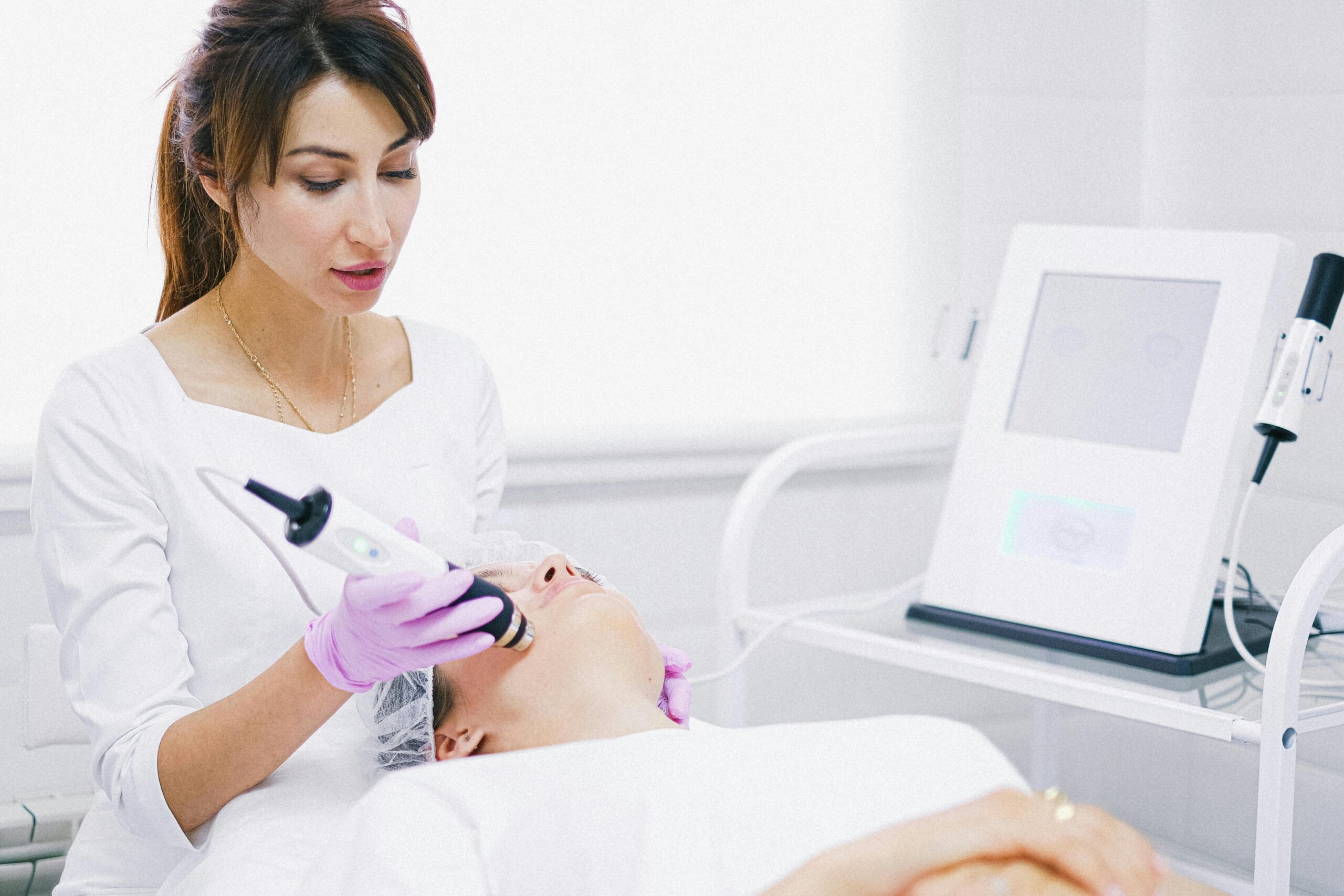 Aesthetician providing a laser facial treatment to a patient in a spa clinic setting.