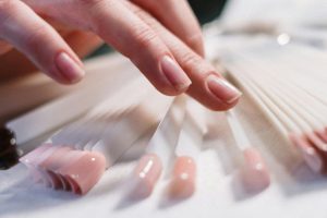 Close-up of a woman's hand selecting nail polish colors in a beauty salon.